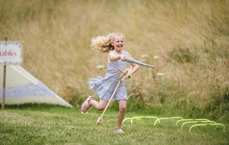 A girl on a hobby horse with a toy lance pretending to joust