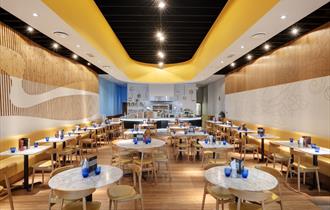 The bright interior of Pizza Express set for diners with chairs, tables with menus and blue glasses on.
