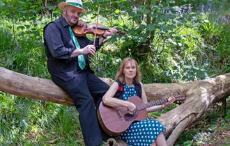 Two musicians sat on a fallen tree in the woods