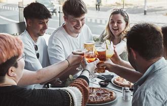 Crowd around a pizza with drinks