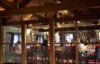 The inside of Miller & Carter with wooden beams, stone walls and diners sat at tables on black and red chairs.