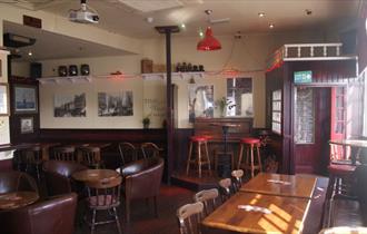 Interior of Admiral McBride showing wooden tables and chairs and walls covered with pictures.