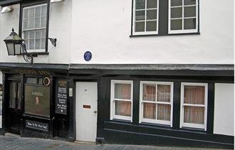 The black and white painted exterior of the Minerva Inn with large lantern hanging outside above the pavement.