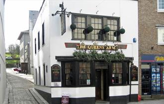 The white and black painted front of the Queens Arms with plant displays above the entrance.