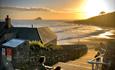 A woman sits with a dog on some steps , the sun sets over the sea in the background