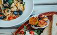 Two plates of food, one showing a seafood and pasta dish and the other showing bread and salad.