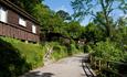 A wooden chalet on a path surrounded by green hedges