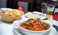 A table set for a meal with a bowl of curry, naan bread in a basket, a plate of rice, a drink and candles.