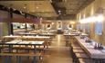 A full length shot of the inside of the brightly lit restaurant showing long tables and benches.
