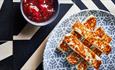 A grey patterned plate with 5 Halloumi sticks and a pot of red chilli jam.