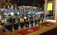 The bar inside Admiral Mcbride showing pumps and displayed bottles with a wooden bar top covered with bar mats.