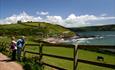 Two walkers lean against a wooden fence looking across a coastal view