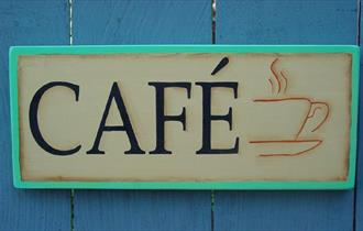 A sign bearing the word CAFE and a picture of a steaming cup of coffee. This hung on a blue painted fence.