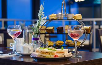 A table set with Afternoon Tea for 2 served on a tiered display with sandwiches, cakes and scones with jam and cream.