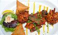 A white plate of different starters including bhajis and samosas with salad and lemon garnish.