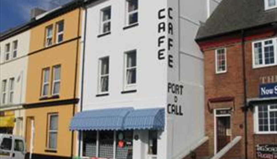 The outside of the Port O'Call Café showing brightly coloured awnings, outdoor tables and chairs and adjacent terraced properties.