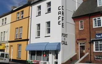 The outside of the Port O'Call Café showing brightly coloured awnings, outdoor tables and chairs and adjacent terraced properties.