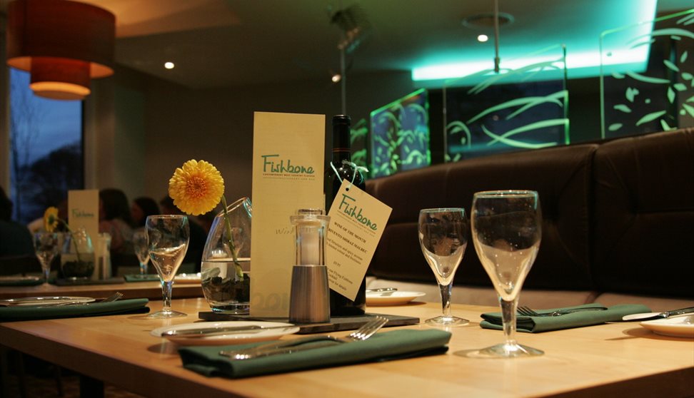 A table set for dinner with glasses, a menu and a yellow flower in a vase.