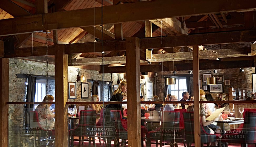 The inside of Miller & Carter with wooden beams, stone walls and diners sat at tables on black and red chairs.