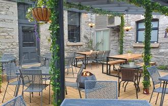 Outside courtyard area with tables and chairs, a fire pit and a plant covered pergola.
