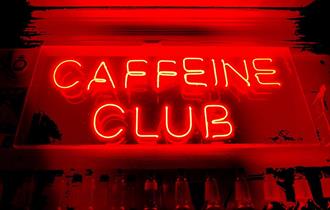 A red neon "Caffeine Club" sign.