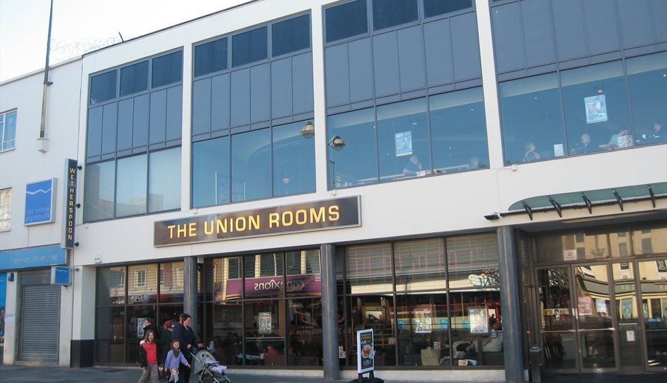 The glass frontage of the Union Rooms on a sunny day with a family and pushchair strolling by in the foreground.