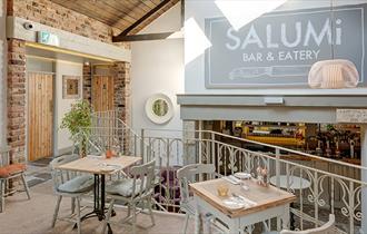 Inside Salumi, showing cream painted walls, tables and chairs, exposed brickwork and cream wrought iron railings separating seating areas.