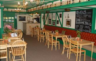 The restaurant interior painted green with wooden tables and chairs and a large menu chalkboard.