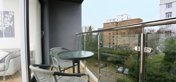 Two chairs and a table on a modern glass balcony overlooking the town centre