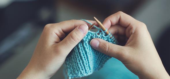 Image shows someone knitting with blue wool.