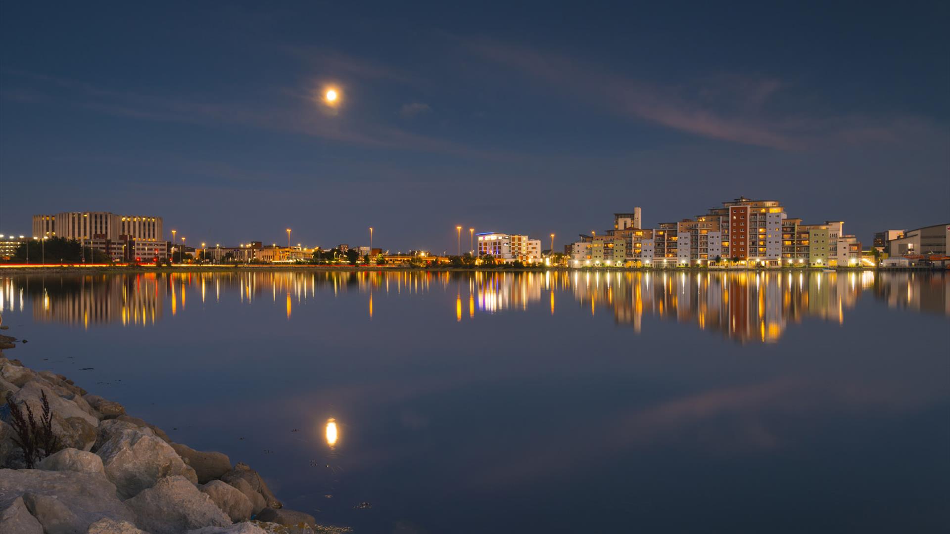 buildings illumintating the night sky and still water at holes bay in Poole