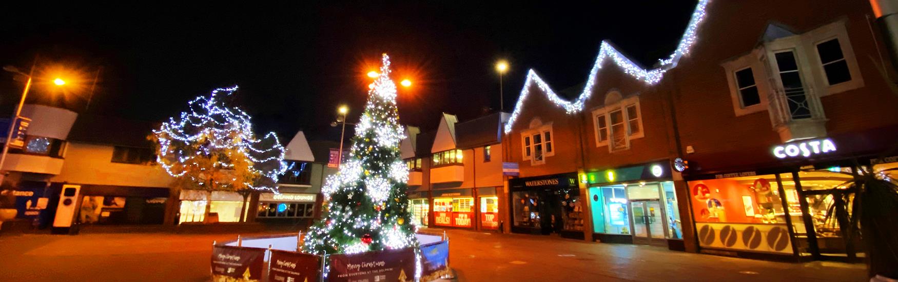 Christmas tree in the middle of the square with decorated lights around it on the houses