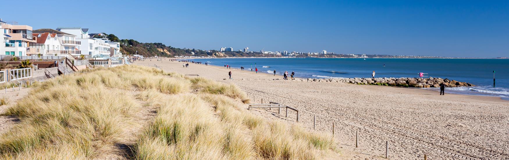Landscape view of Sandbanks Beach with buildings on the left hand side and sandy beach on right with sea in background