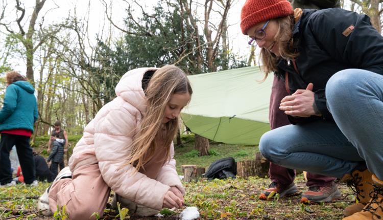 Mother watching daughter learning how to light a fire.