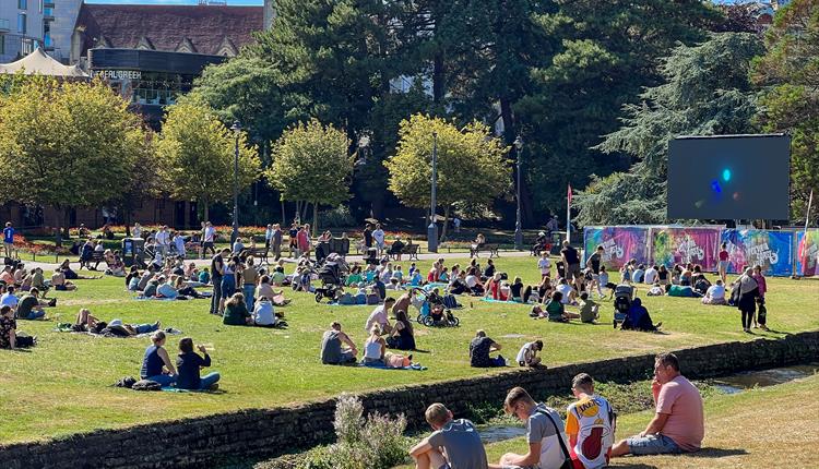 Image of a big screen placed on a green area with trees and grass.