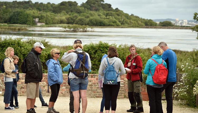 People gathered with walk leader with Brownsea lagoon and trees in the background.n