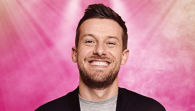 Image of a man smiling with a pink background and lights behind.