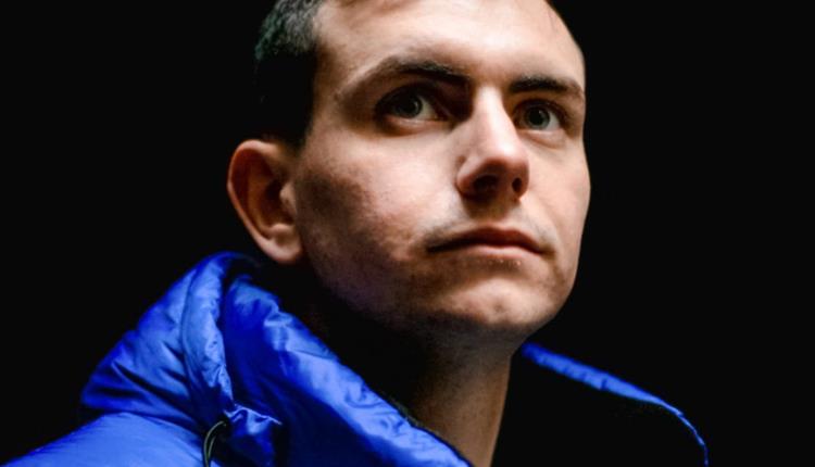 Image of the performer Connor Burns from the shoulders up in a blue puffer jacket against a black background