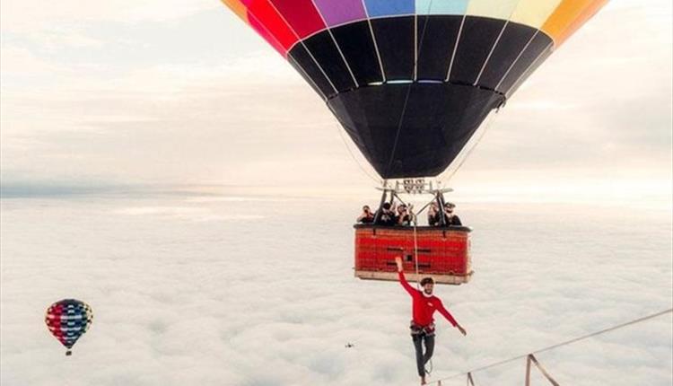 Picture of a colourful balloon in the air with a man walking the tightrope
