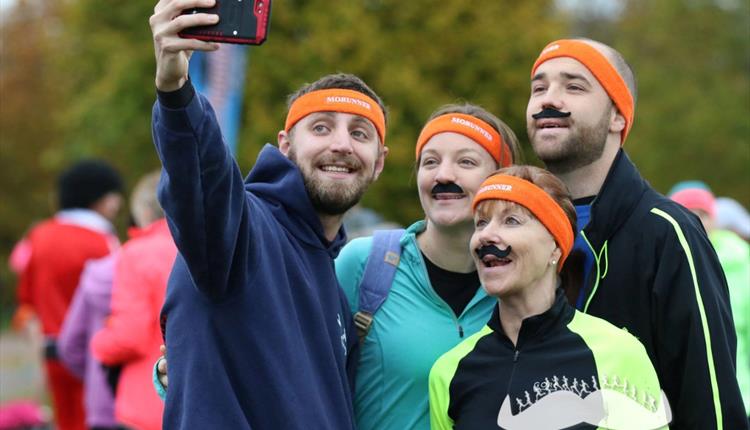 Picture of two men and two women in running clothes and orange Mo Run headbands and moustaches taking a selfie