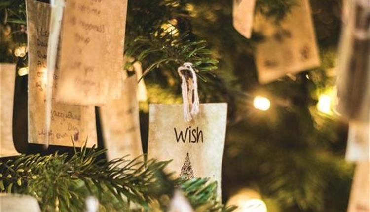 A close-up of a Christmas tree with fairy lights and a note decoration with a written wish on.