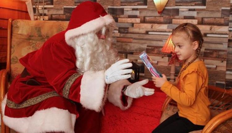 Father Christmas sitting down opposite a little girl giving her a gift
