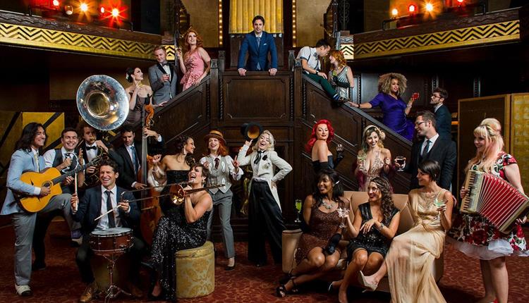 Image of performers sitting or standing playing instruments dancing, posing, dressed in theatrical costume, on stairs and infront of stairs
