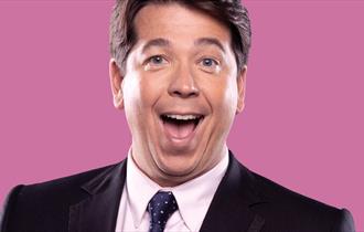 Image of man smiling with a pink background behind him.