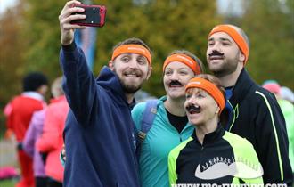 Picture of two men and two women in running clothes and orange Mo Run headbands and moustaches taking a selfie