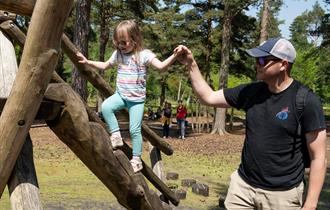 Father holding his daughter's hand while she climbs on the natural play area.