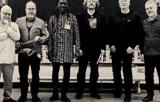 Six artists of Thokozile Collective standing against a classroom backdrop