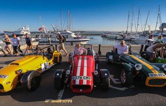 Yellow, red and green roadster style cars lined up at Poole quay with harbour behind them