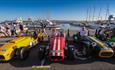 Yellow, red and green roadster style cars lined up at Poole quay with harbour behind them