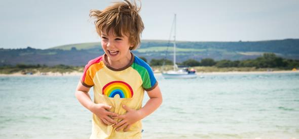 Boy laughing and playing at the beach, sea and boat in the background